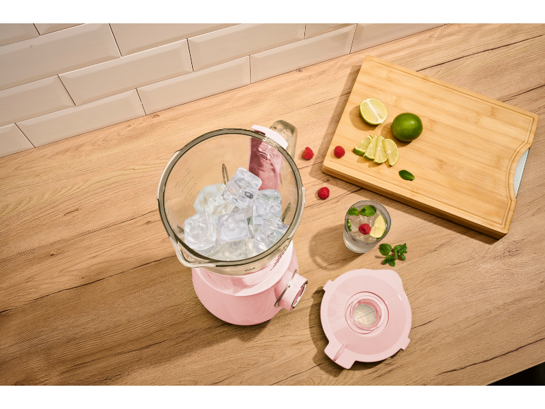 Roze blender sa ledom, čaša pića, voće i drvena daska za sečenje.