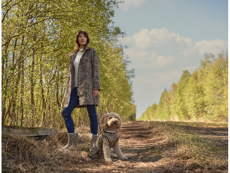 Žena i pas u kaputima sa leopard printom na šumskoj stazi
