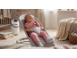 Beba u ležaljci, sa kantom za pelene i ćebadima u pozadini.