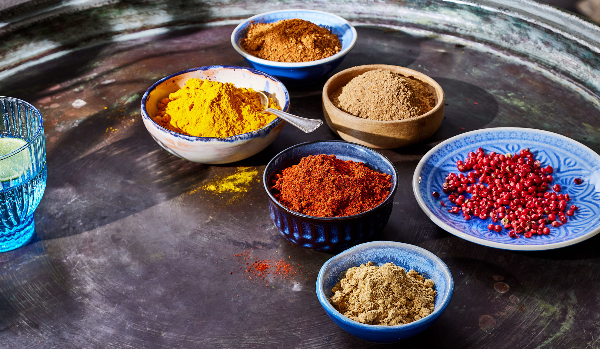 Različiti začini u činijama: kurkuma, paprika, biber i ostali na metalnom poslužavniku.