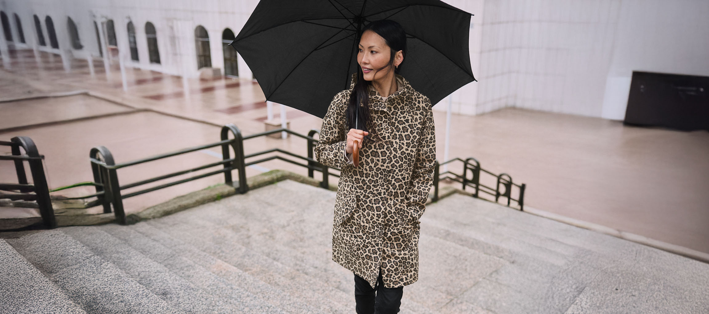 Žena u kaputu sa leopard printom sa kišobranom na stepenicama.
