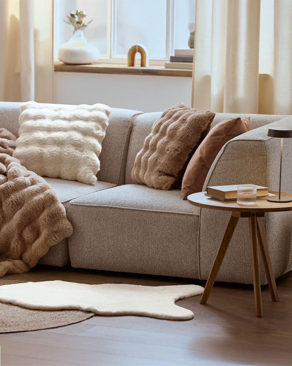 Siva modularna sofa sa pufnastim jastucima i ćebadima, drveni pomoćni stočić.