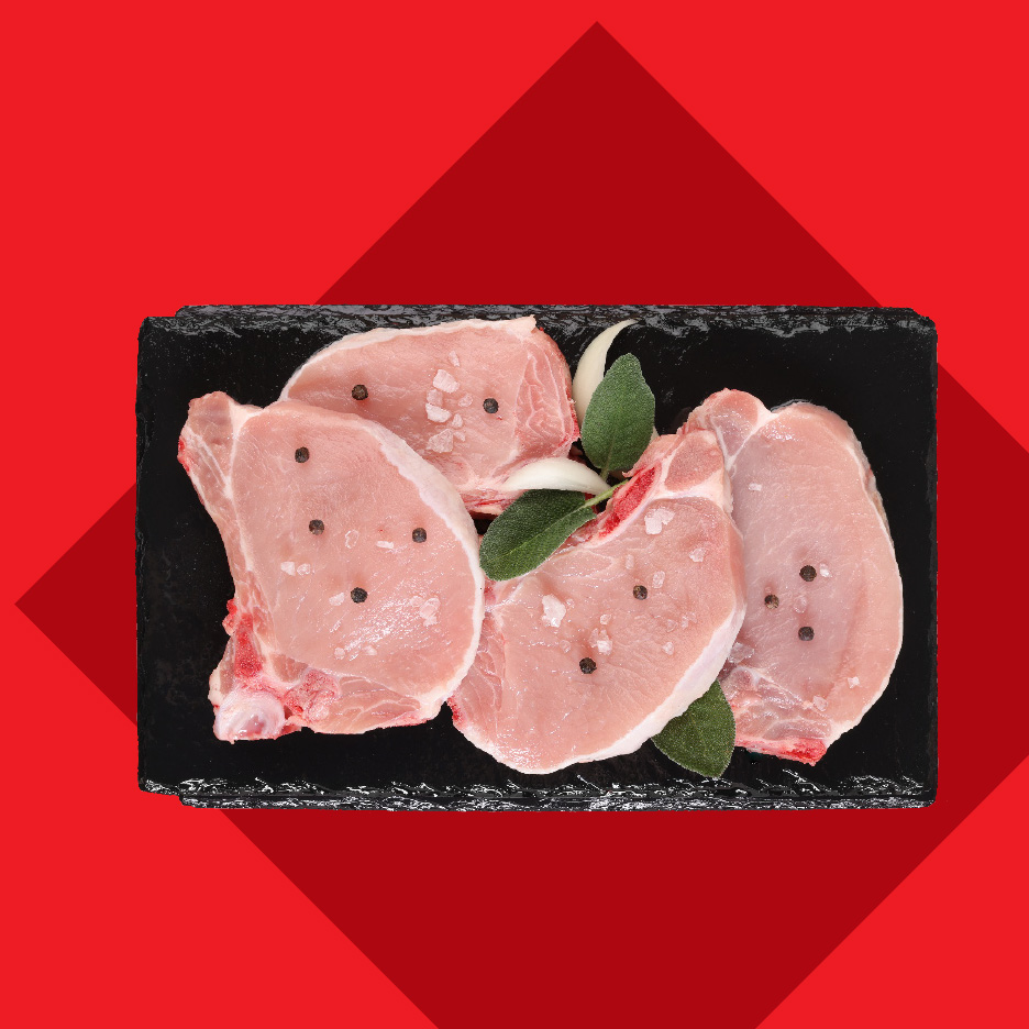 Sveži svinjski kotleti sa biberom, solju i začinskim biljem na crnoj ploči.