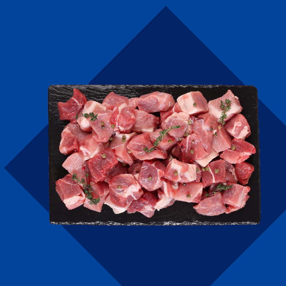 Sveže isečeno svinjsko meso na crnoj dasci, posuto začinima.