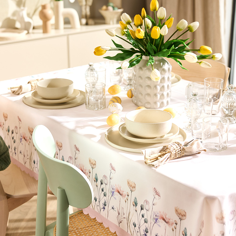 Uskršnja trpeza sa belim stolnjakom sa cvetnim dezenom, bež posuđem i vazom sa žutim i belim lalama.