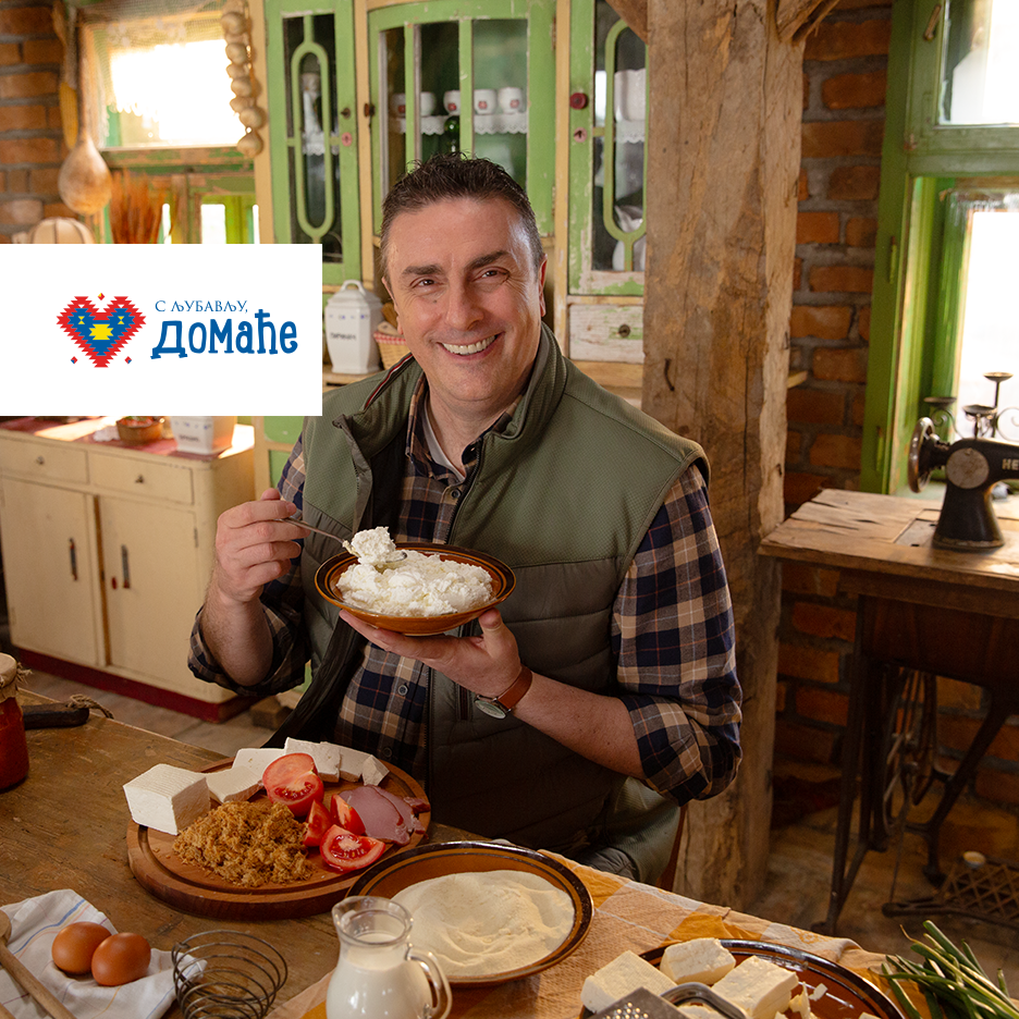 Muškarac jede sir, sa sirom, paradajzom i mesom na stolu. Logo: „С љубављу, ДОМАЋЕ“.