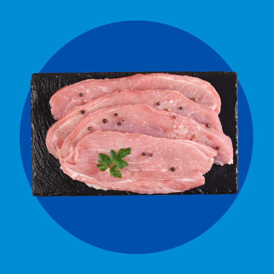 Sveži svinjski odresci sa biberom i peršunom na crnoj ploči.