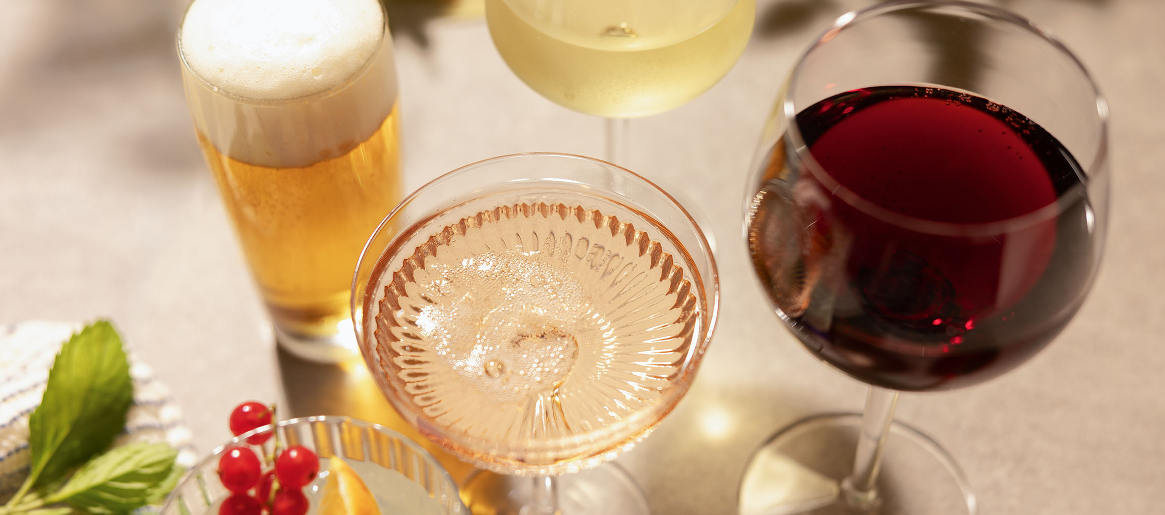 Pivo, roze vino i crveno vino u čašama, sa bobicama i mentom.