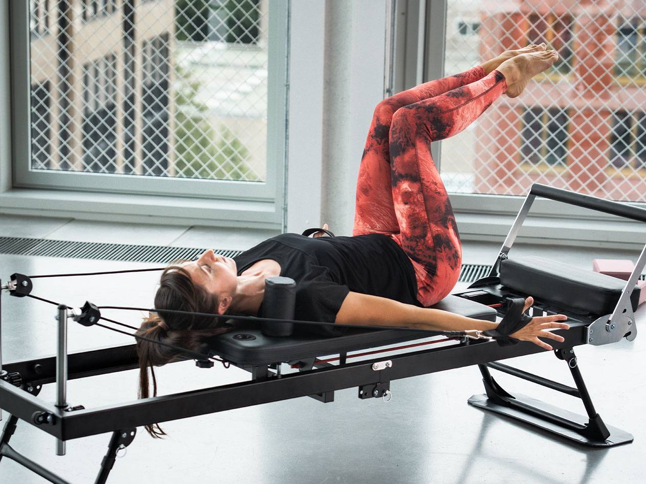 Žena radi Pilates na reformer spravi, u crvenim i crnim helankama