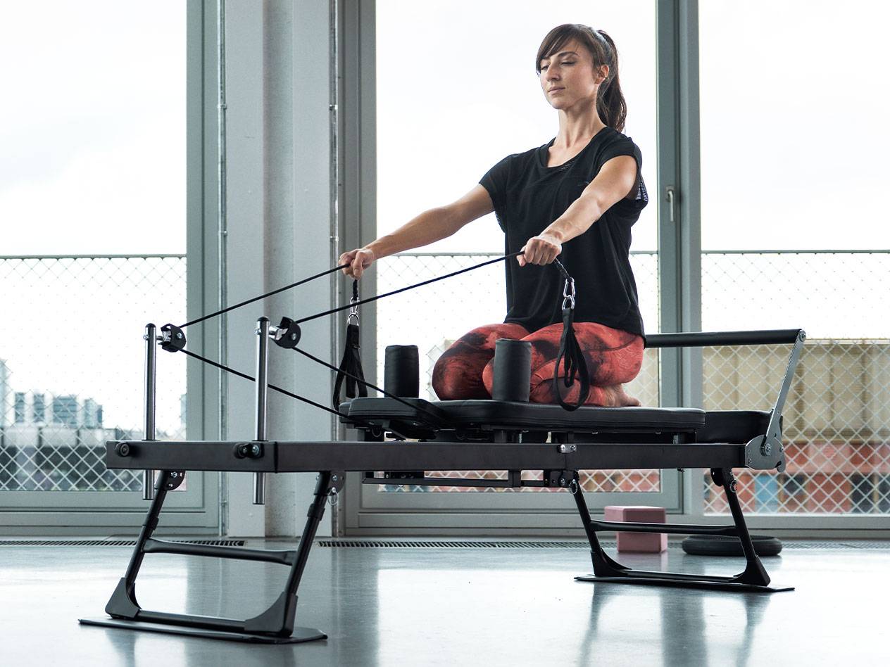 Žena vežba Pilates na reformer spravi sa velikim prozorima u pozadini.
