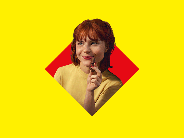 Nasmejana riđokosa žena drži čokoladu na žutoj i crvenoj pozadini.