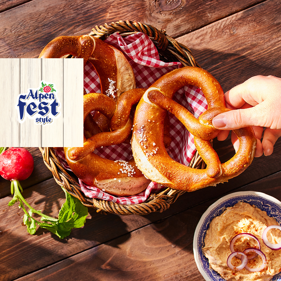 Perece u korpi sa crvenim kariranim ubrusom, ruka uzima jednu, sa namazom i rotkvicom. Logo: Alpen Fest style.