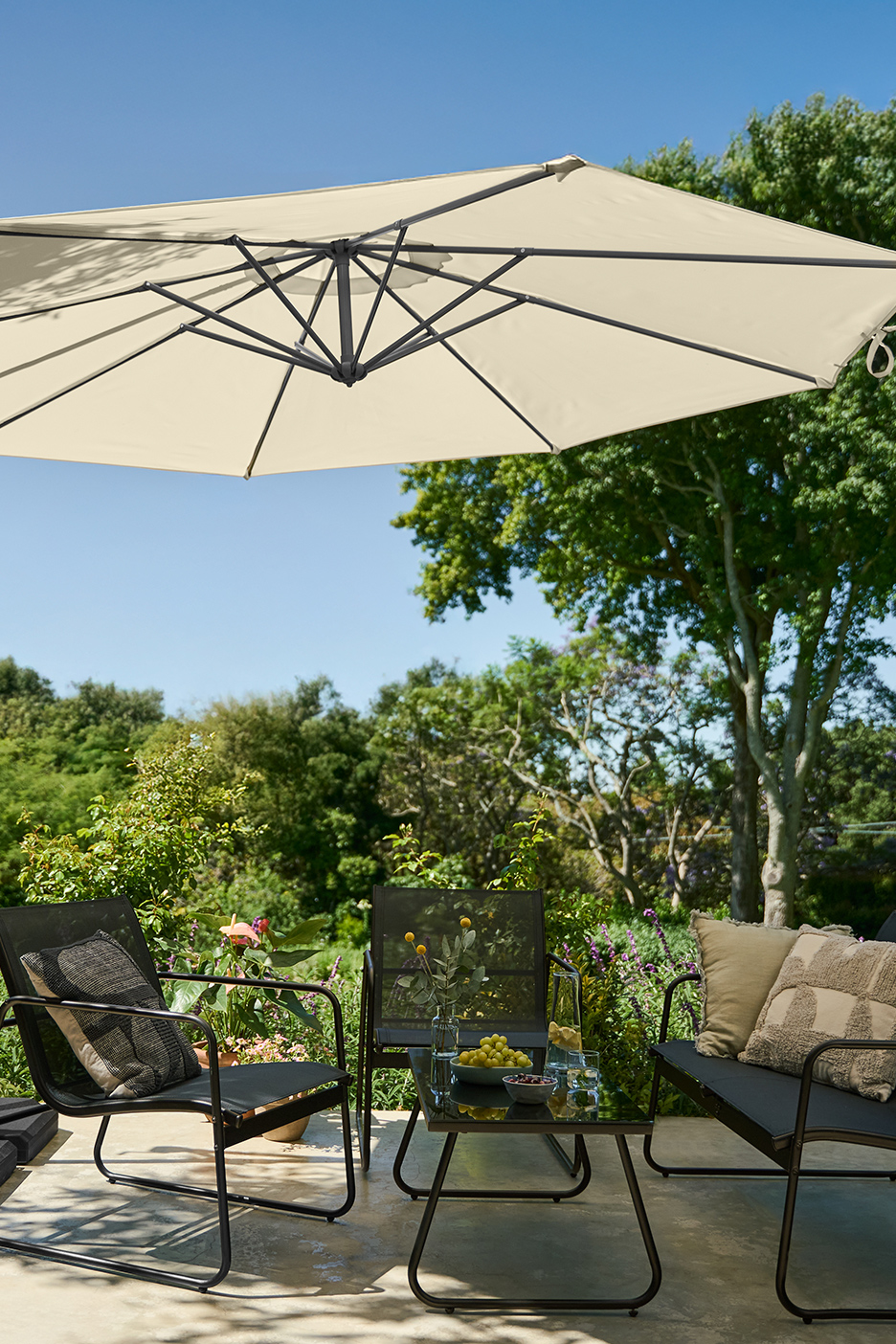 Baštenski set sa suncobranom, stolom i stolicama, okružen zelenilom.