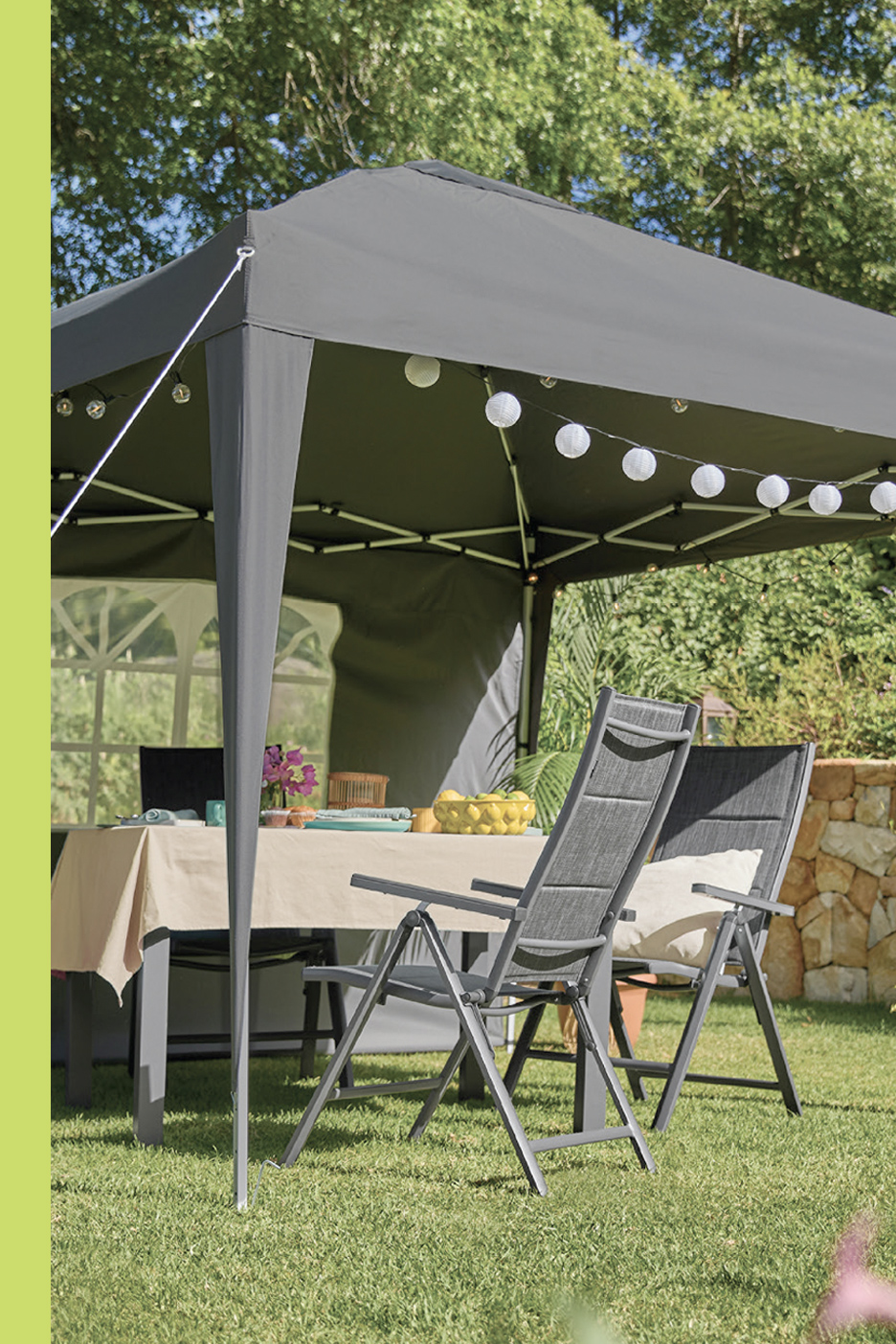 Sivi baštenski šator sa stolom, stolicama i ukrasnim svetlima u bašti.