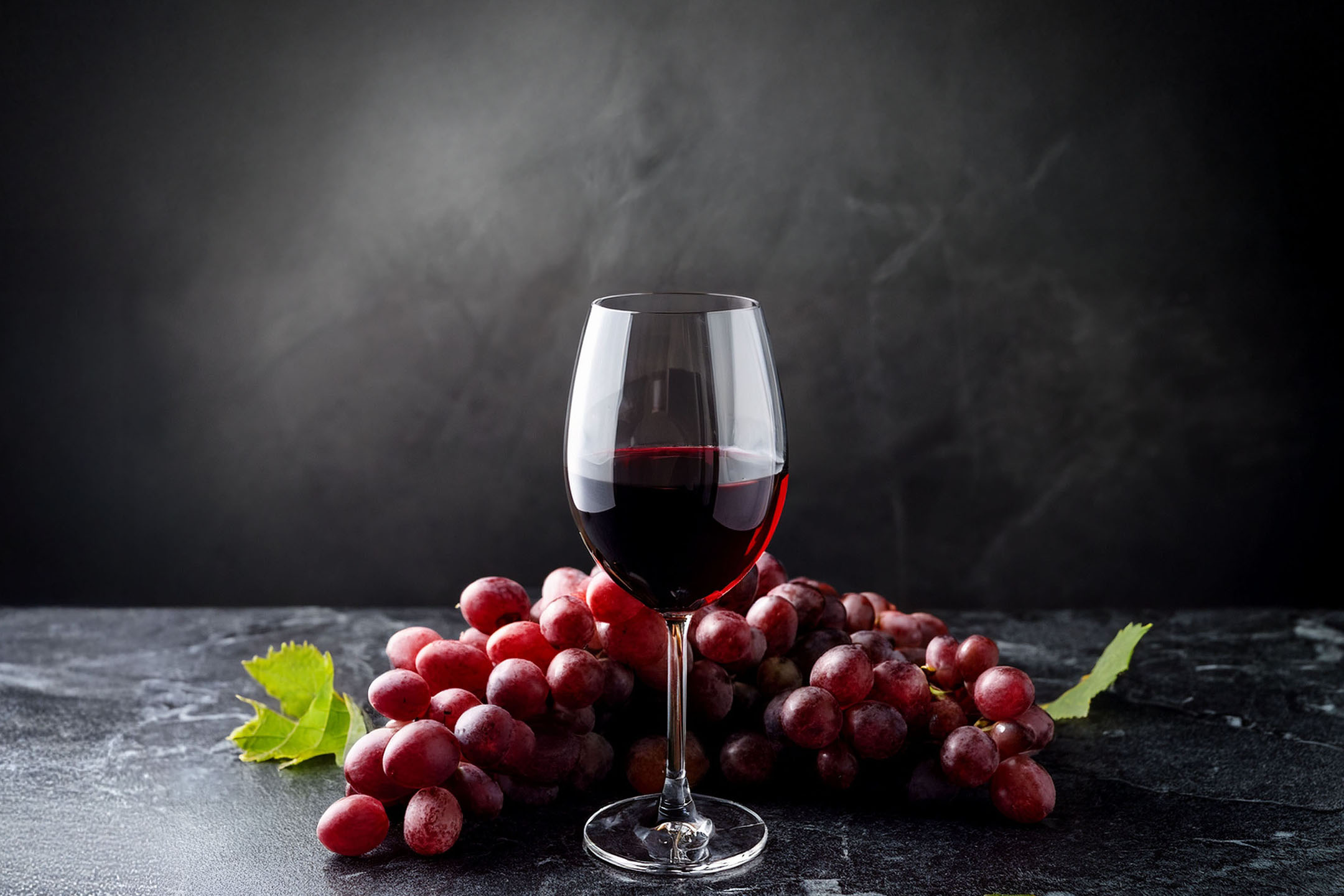 Čaša crvenog vina i grozd crvenog grožđa na tamnoj pozadini.