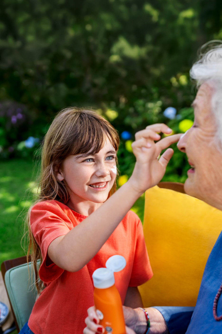 Devojčica nanosi kremu za sunčanje na nos starije žene u bašti.