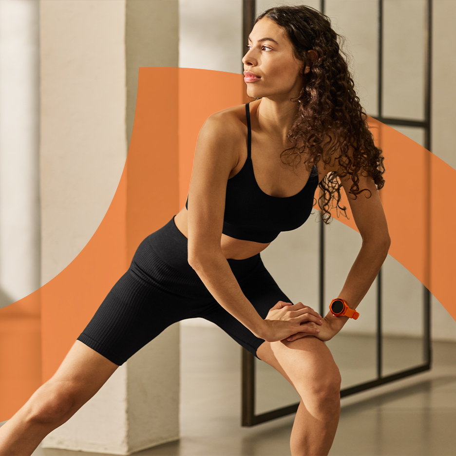Žena u crnom sportskom grudnjaku i biciklističkim šortsevima isteže se, nosi narandžasti pametni sat.