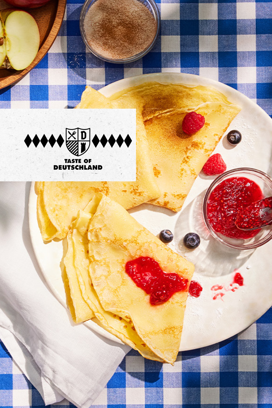 Palačinke sa džemom od malina, borovnicama i šećerom na plavo-belom kariranom stolnjaku. Tekst: Taste of Germanland.