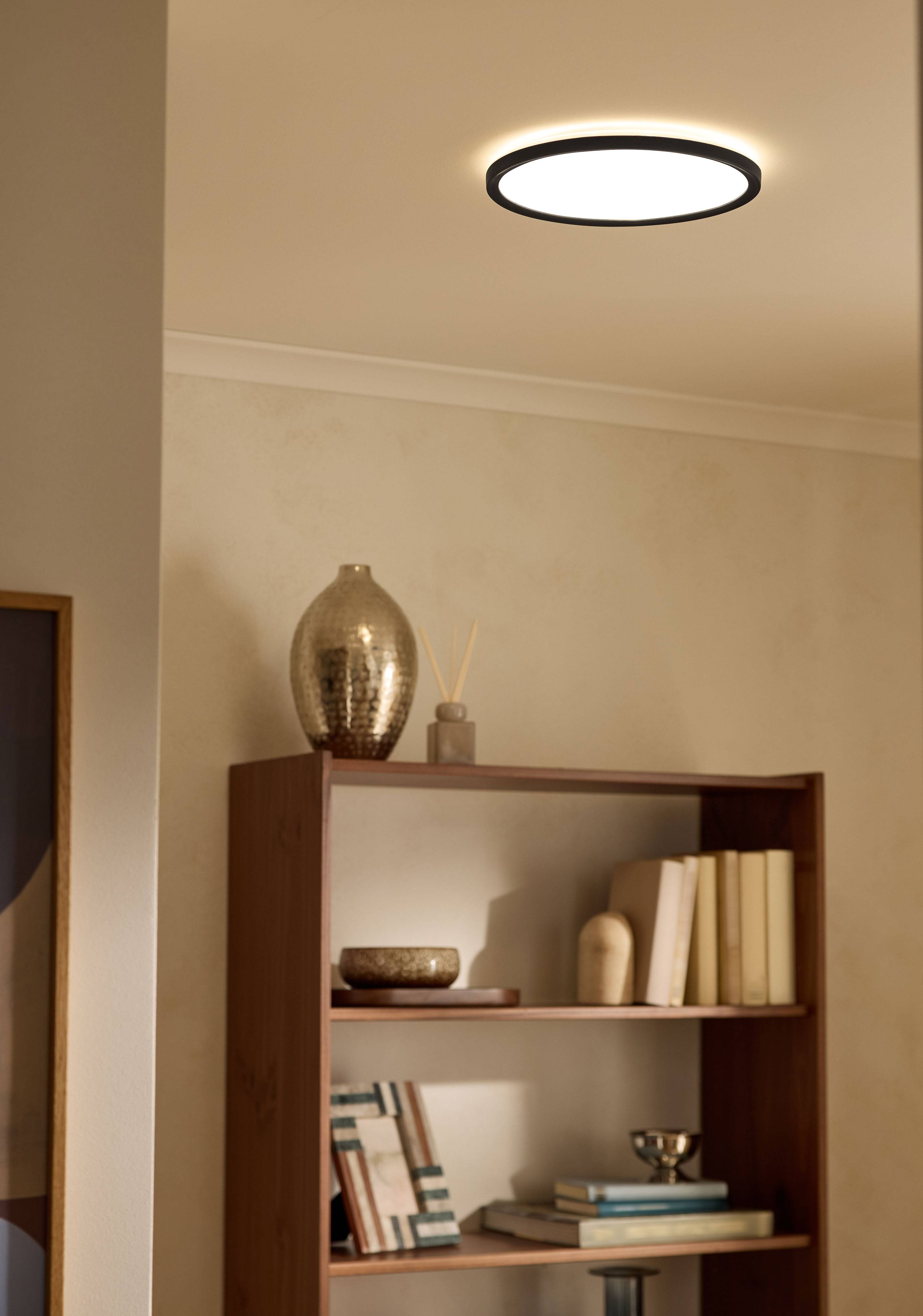 Plafonska lampa osvetljava policu za knjige u dnevnoj sobi sa knjigama i dekorom.
