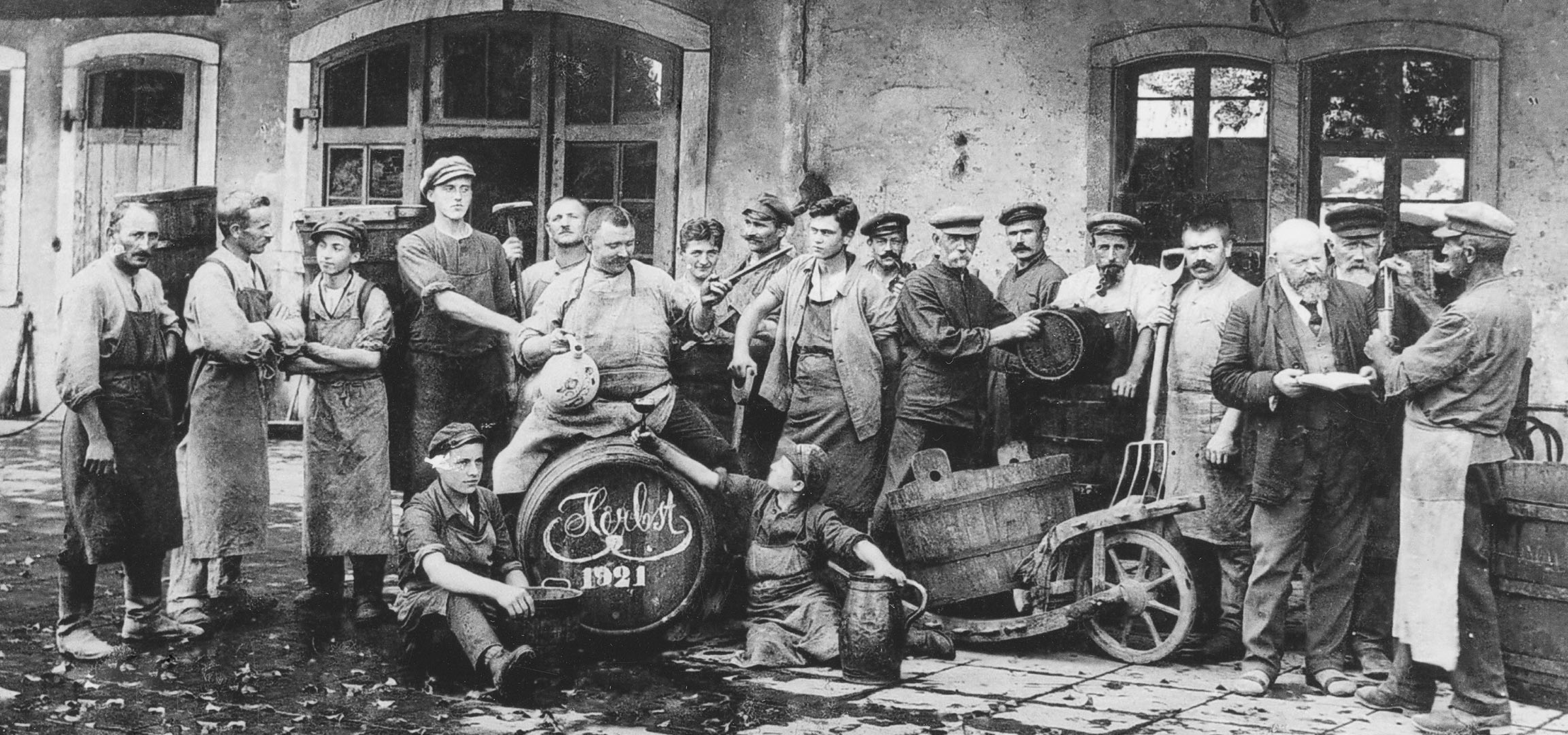 Мушкарци у подруму са винским бурадима, један подиже чашу.