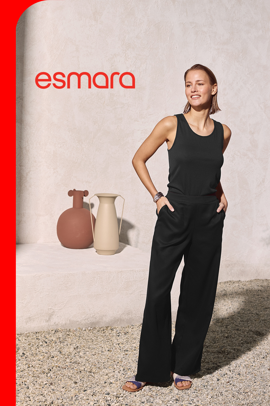Žena u crnoj majici bez rukava i širokim crnim pantalonama, sa vazama u pozadini.