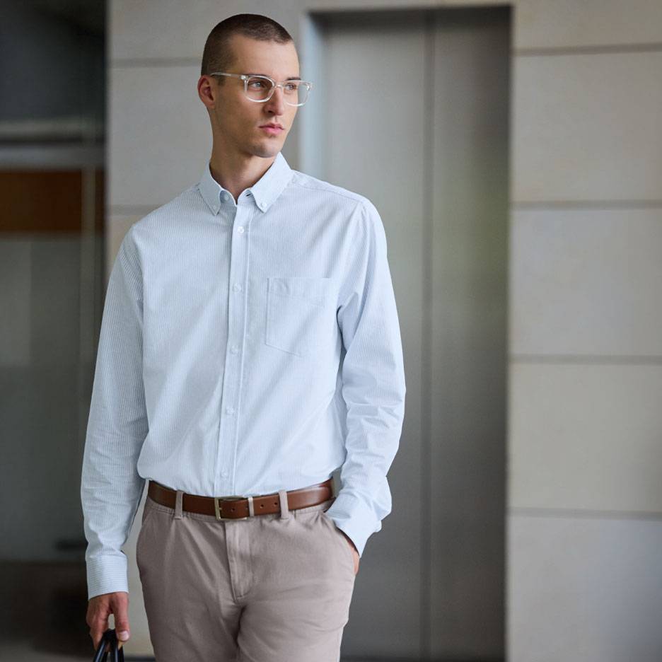Muškarac u svetloplavoj prugastoj košulji i bež pantalonama sa braon kaišem.