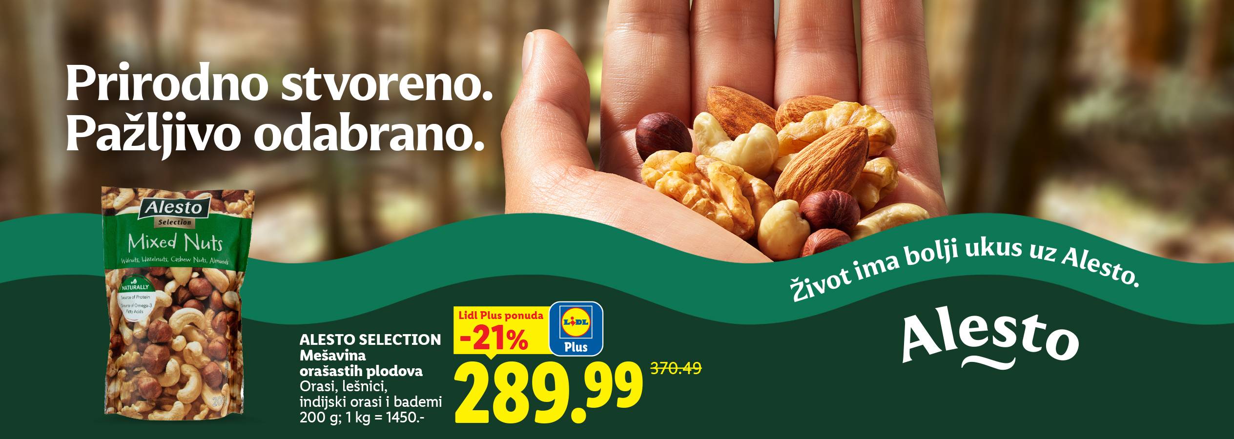 Ruka drži mešavinu orašastih plodova, uključujući bademe, indijske orahe i lešnike, sa pakovanjem mešanih orašastih plodova u prvom planu.