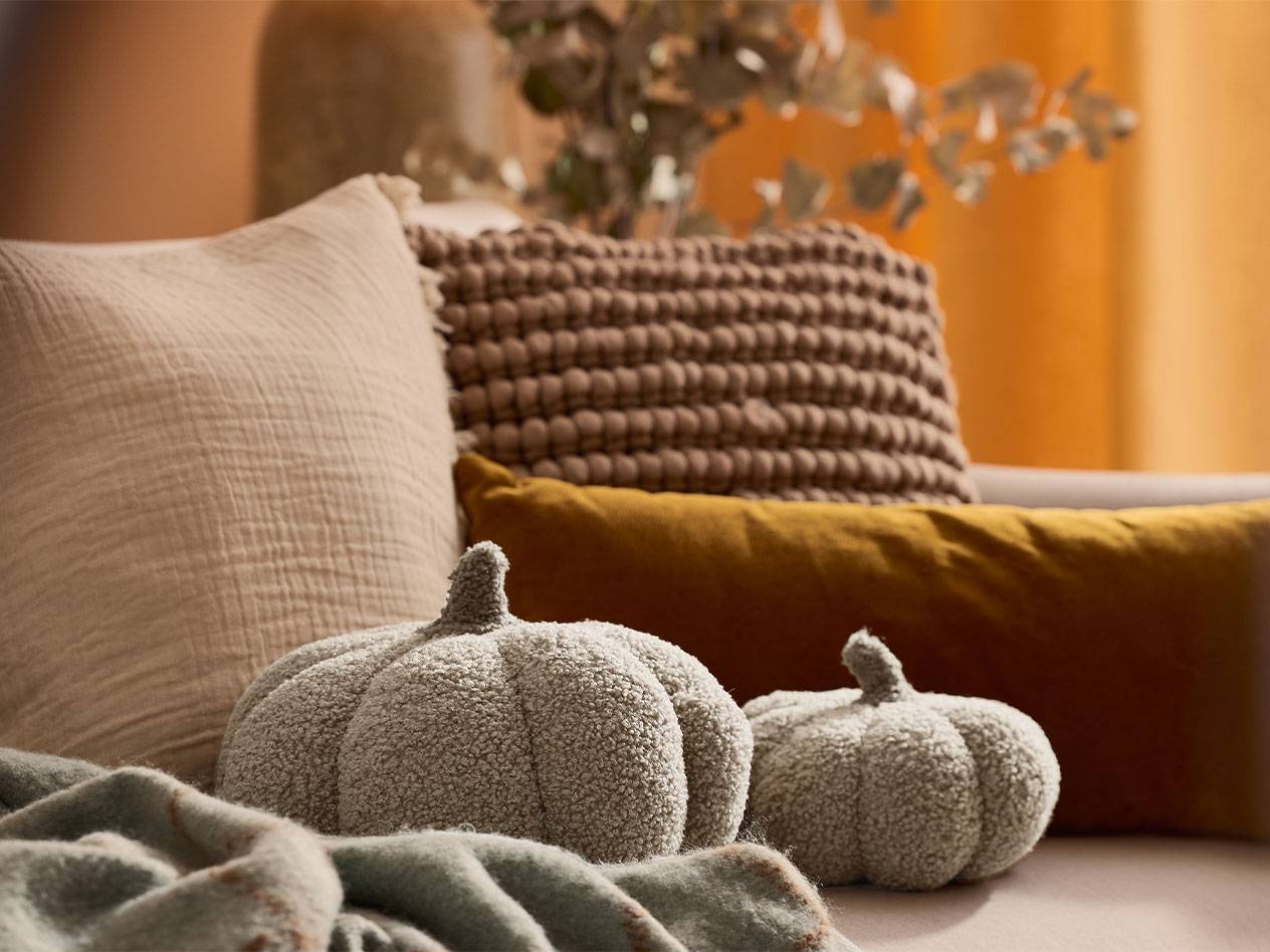 Dve plišane ukrasne bundeve i jastuci u zemljanim tonovima na sofi.