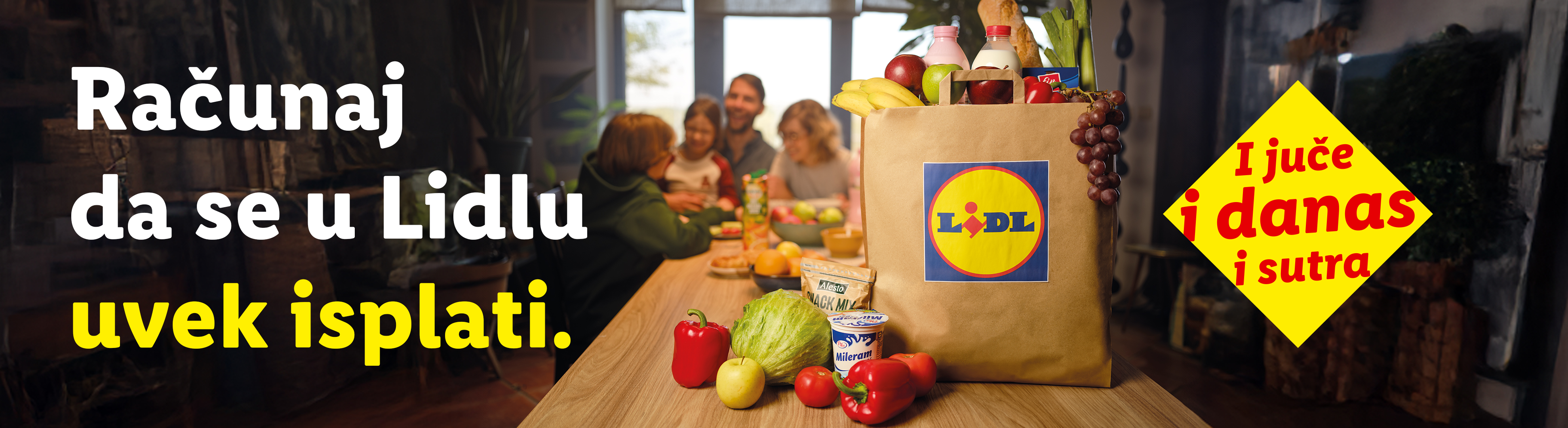Lidl torba puna namirnica, uključujući voće, povrće i mlečne proizvode, sa porodicom u pozadini.
