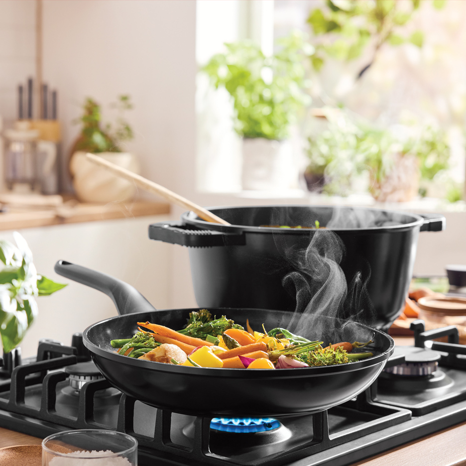 Tiganj i lonac sa povrćem na šporetu u kuhinji.