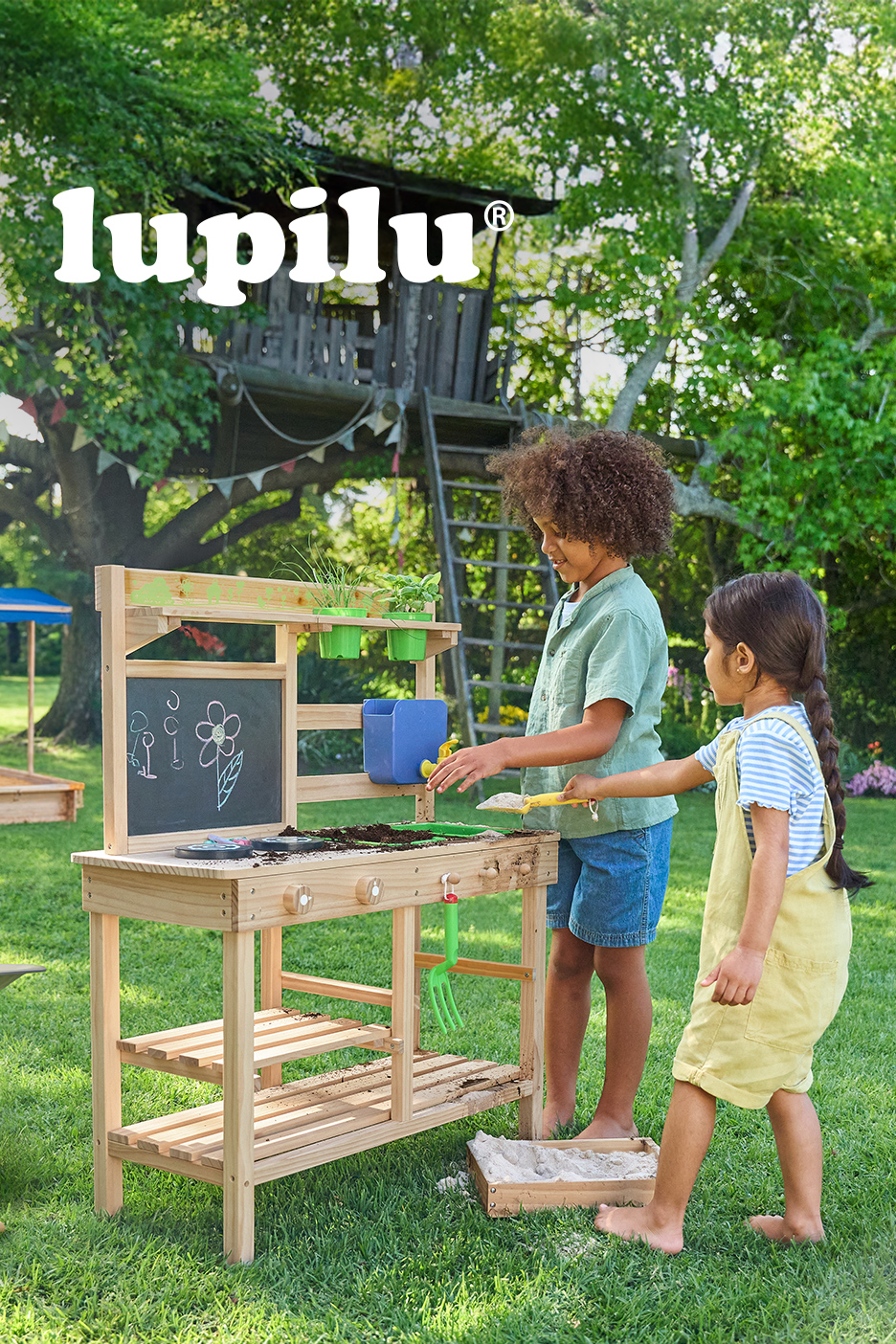 Dvoje dece se igra sa drvenim stolom za igru u bašti, sa tablom i biljkama.