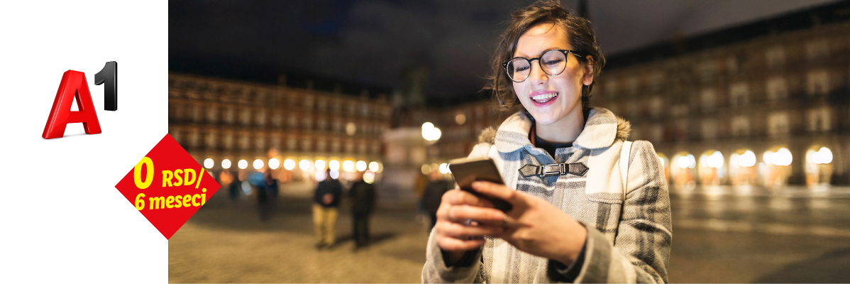 A1 promocija: 0 RSD za 6 meseci. Žena koristi mobilni telefon na noćnom trgu.