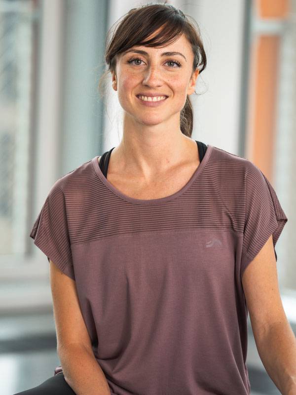 Nasmejana žena u ljubičastom sportskom topu kratkih rukava.