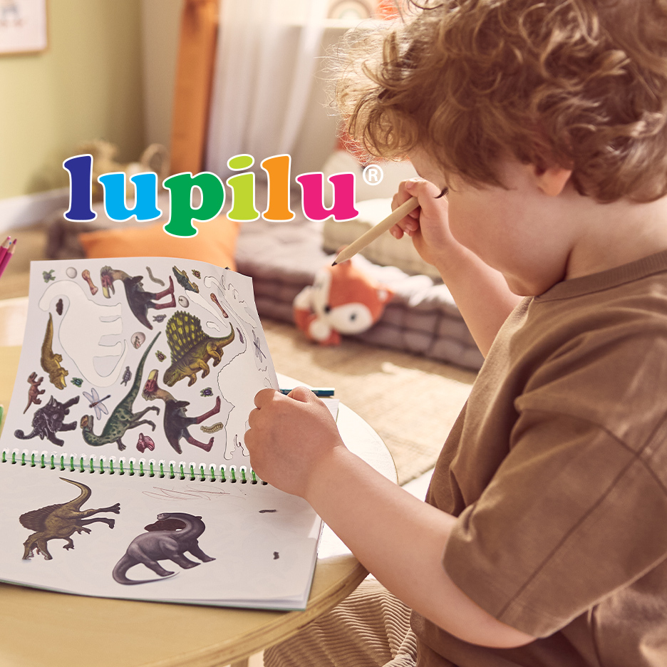 Dečak crta u svesci sa nalepnicama dinosaurusa, držeći olovku.