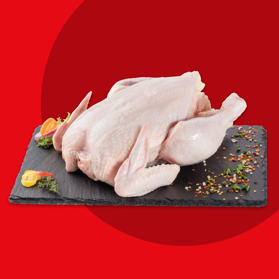 Sveže celo pile na crnoj ploči sa začinima i povrćem na crvenoj pozadini.