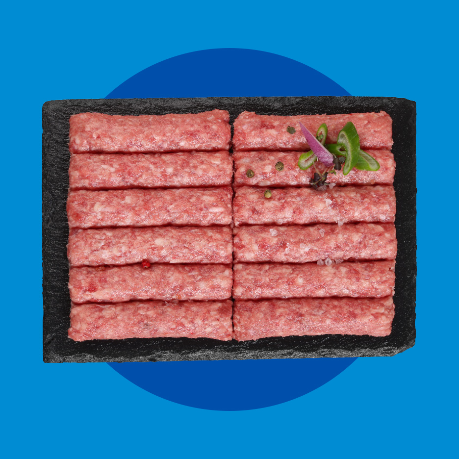 Sveži ćevapi na crnoj ploči, ukrašeni začinima i zelenim papričicama.