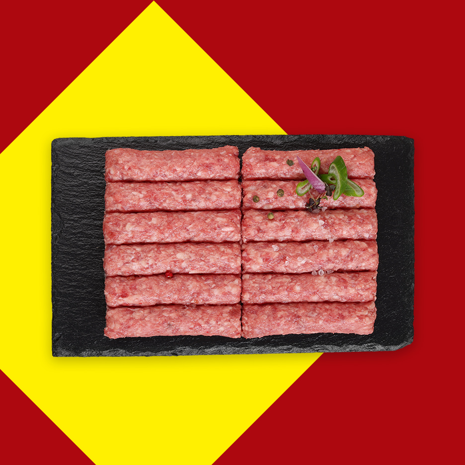 Sveži ćevapi na crnoj ploči, ukrašeni začinima, na žuto-crvenoj pozadini.