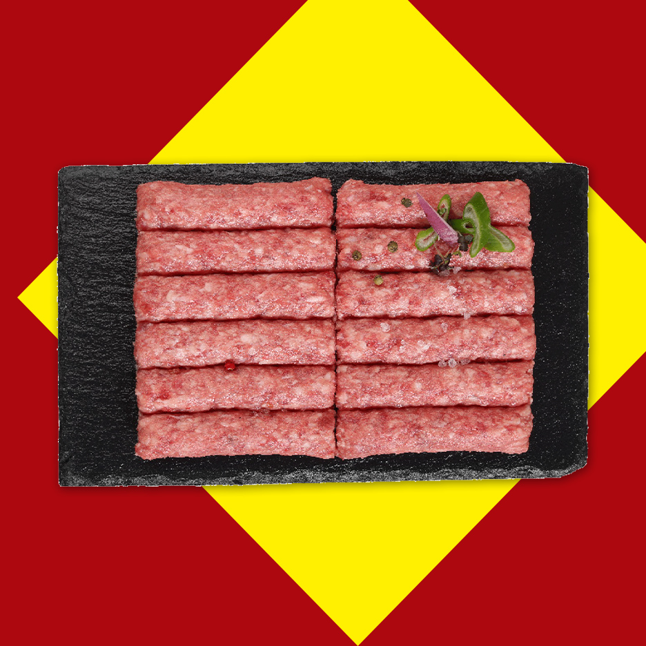 Sveži ćevapi na crnoj ploči, ukrašeni začinima, na crveno-žutoj pozadini.