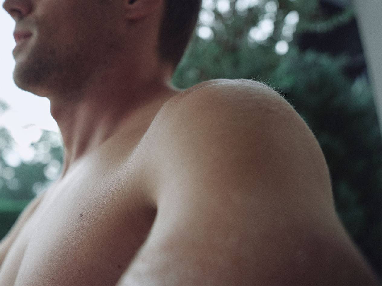 Krupni plan muškog ramena i vrata, sa zamagljenom zelenom pozadinom.