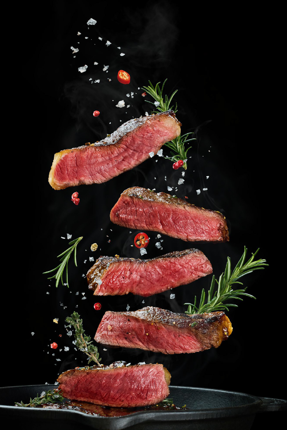 Odresci govedine sa ruzmarinom, čilijem i solju u padu iznad tiganja.