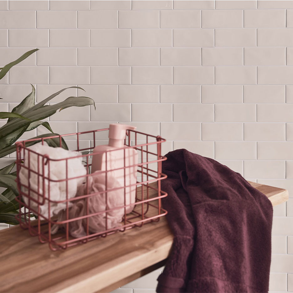 Dekor kupatila sa belim pločicama, drvenom klupom, korpom sa sapunom i peškirima.