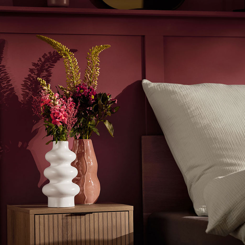 Dve vaze sa cvećem na noćnom ormariću pored kreveta sa belim jastukom.