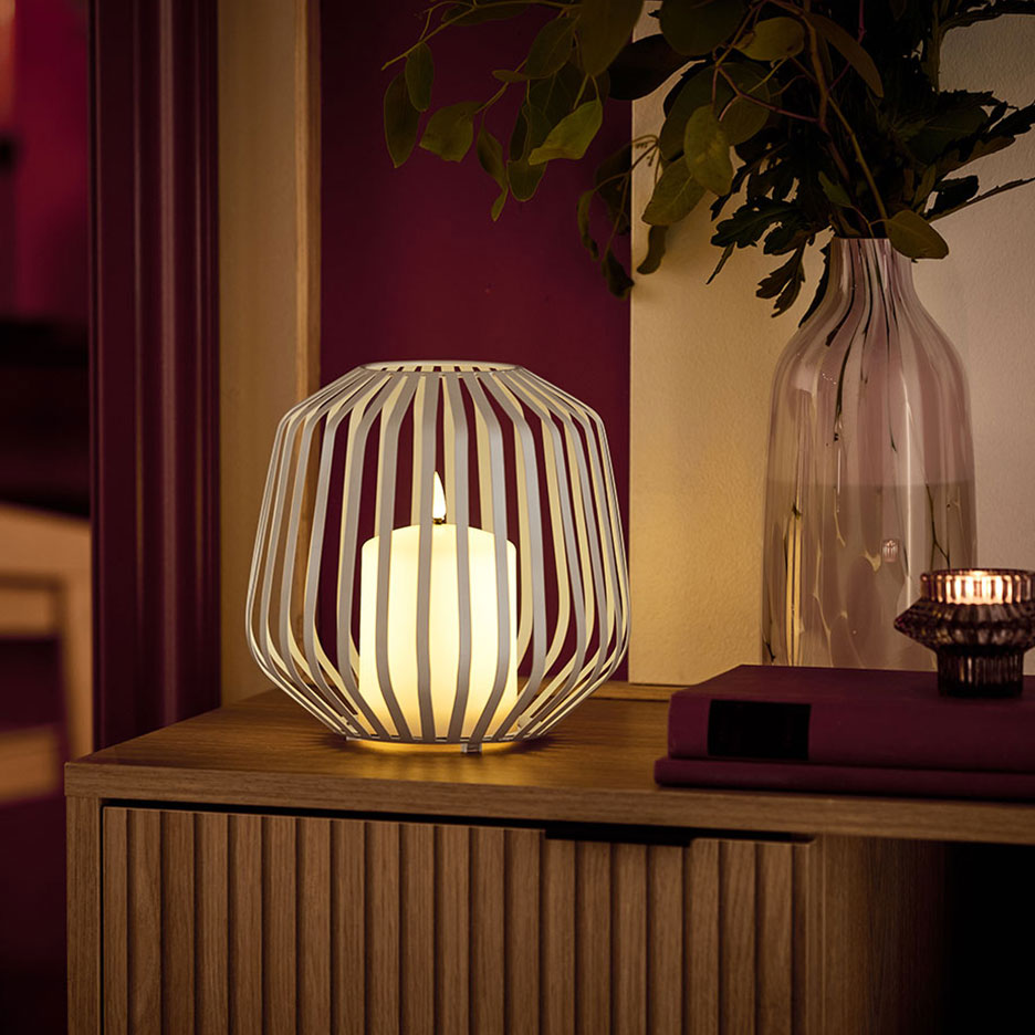 LED sveća u belom metalnom držaču na drvenoj komodi.