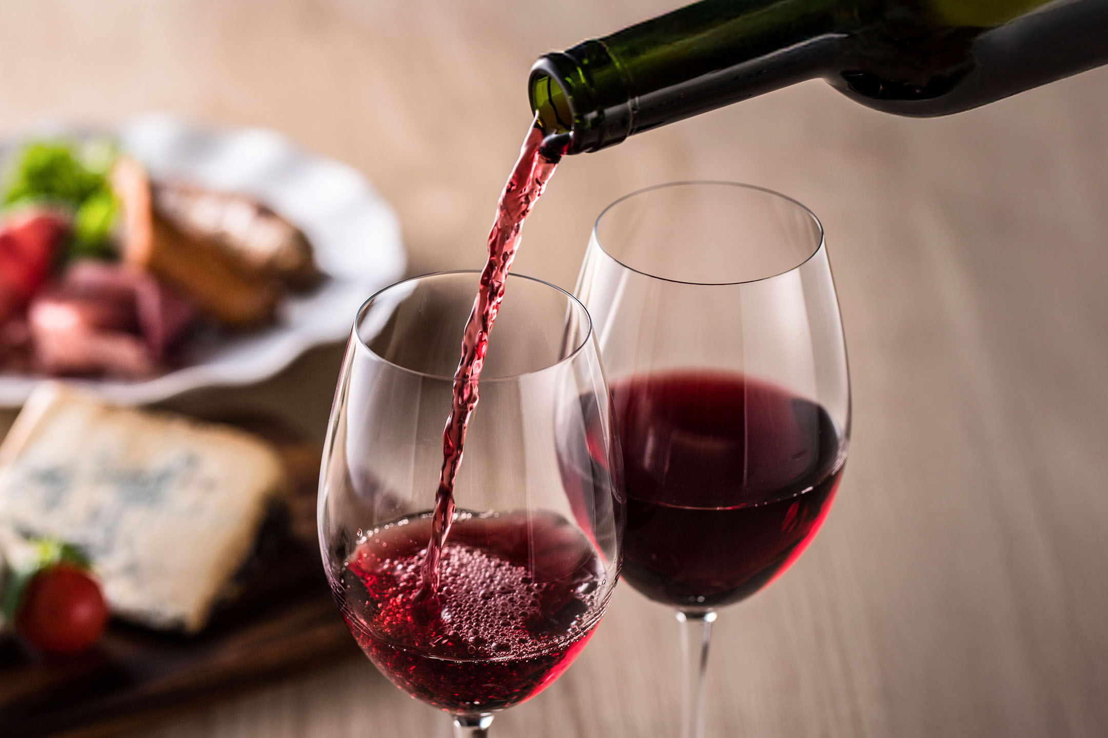 Crveno vino se sipa u čašu, sa predjelima u pozadini.