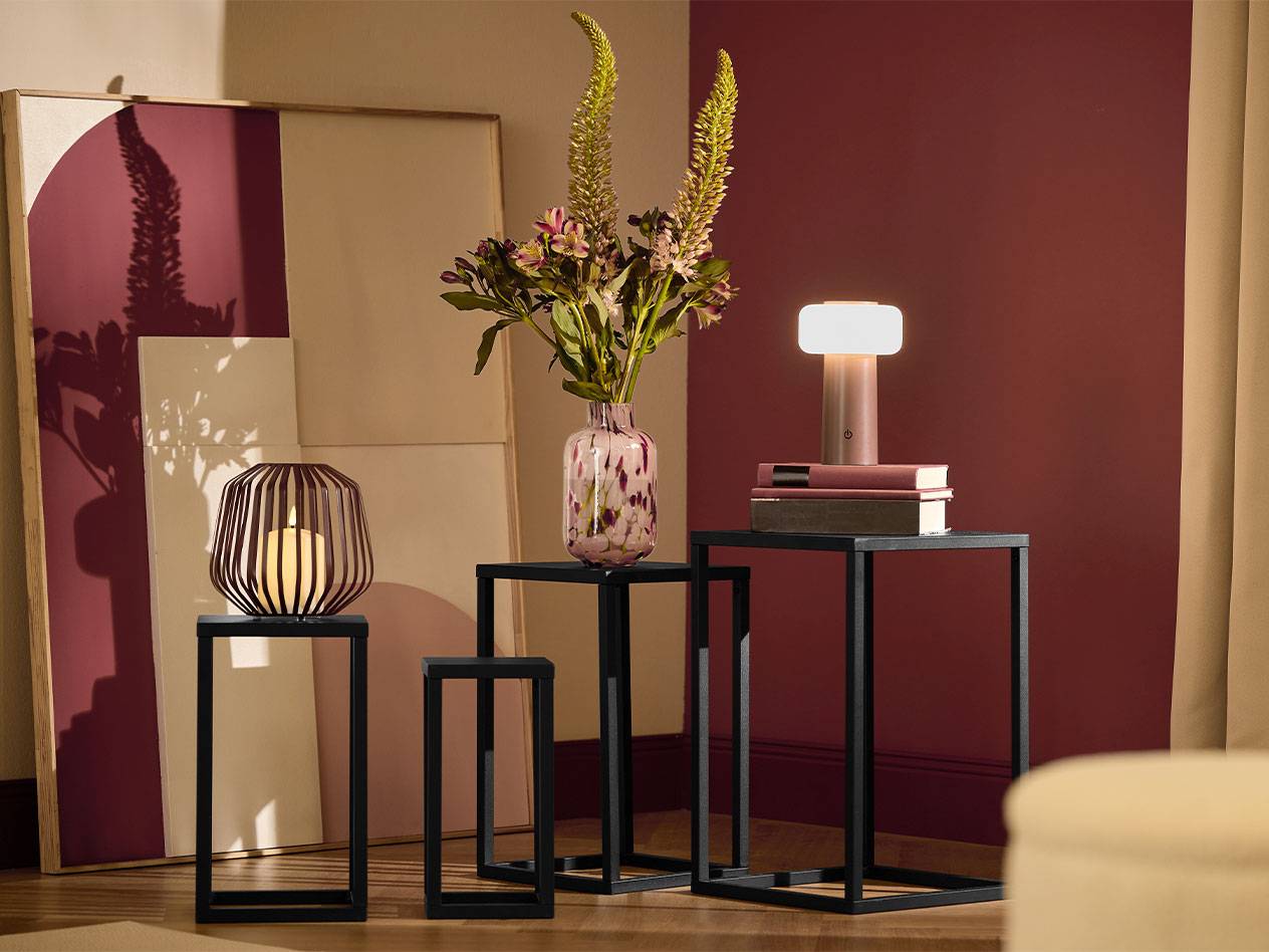 Tri crna pomoćna stola sa svećom, vazom cveća i lampom.