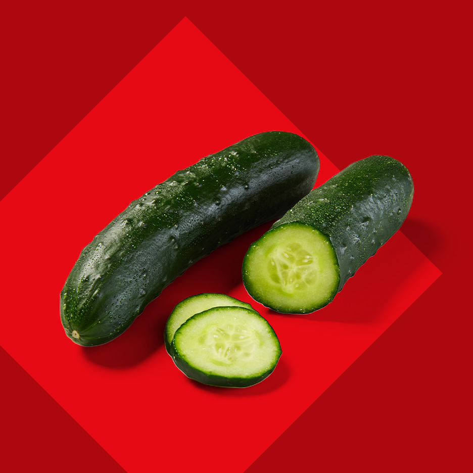 Sveži krastavci, jedan ceo i jedan isečen na kolutove, na crvenoj pozadini.