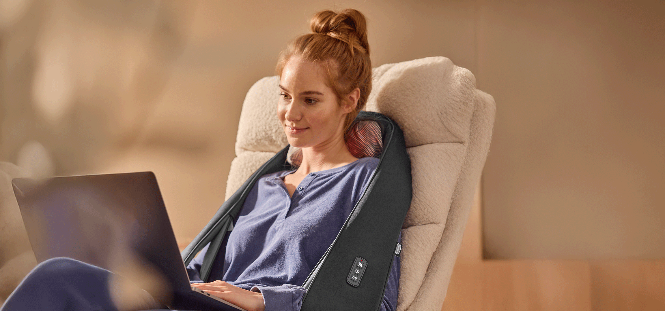 Žena koristi masažer za vrat dok radi na laptopu, druga žena koristi ručni masažer za leđa.