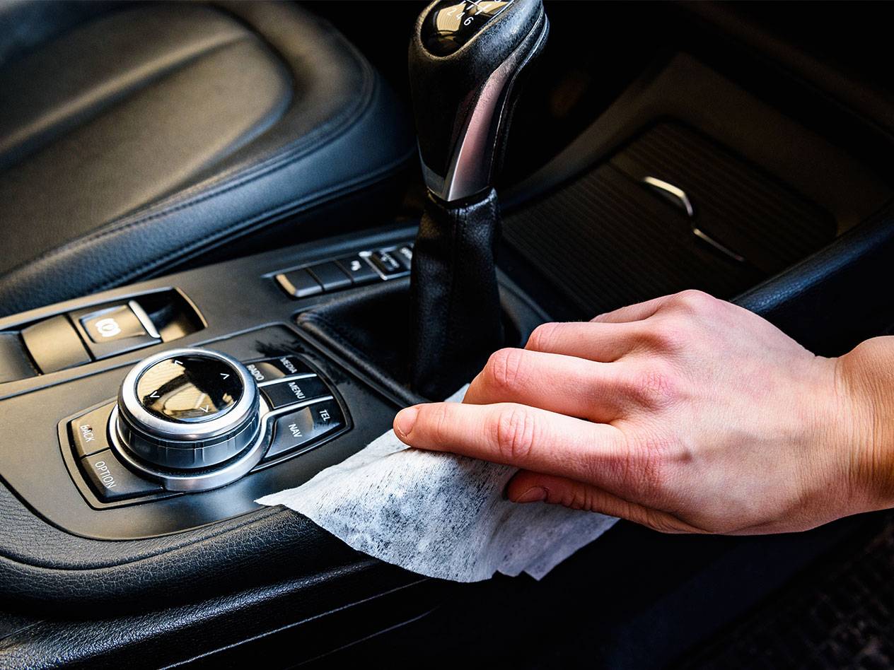 Ruka čisti unutrašnjost automobila vlažnom maramicom.