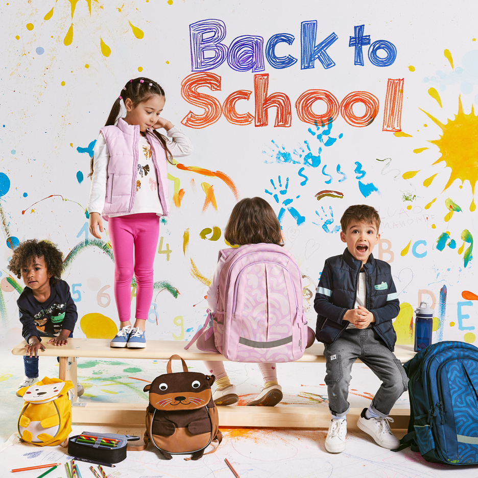 Četvoro dece sa rančevima i školskim priborom, sa tekstom „Back to School“ na šarenoj pozadini.