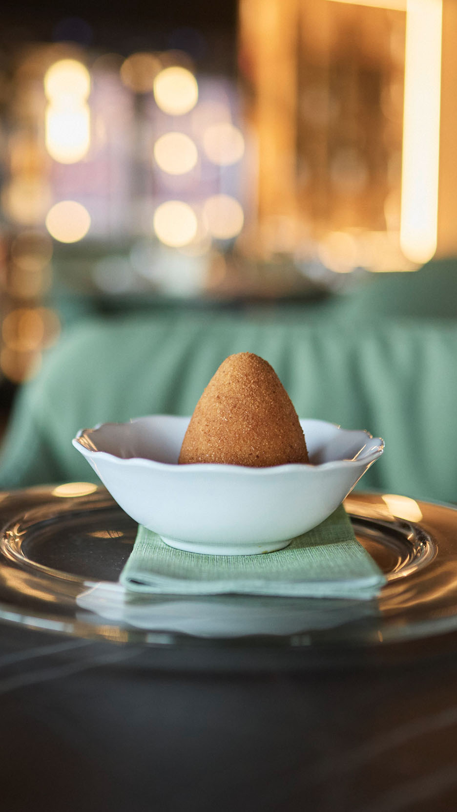 Zlatni arancini u beloj činiji na zelenoj salveti i staklenom tanjiru.